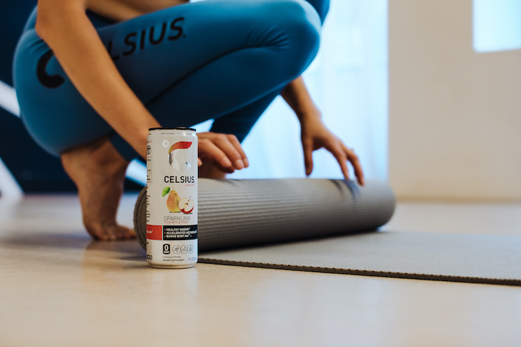 image of a woman rolling out a yoga mat wearing celsius apparel behind a can of sparkling fuji apple pear celsius